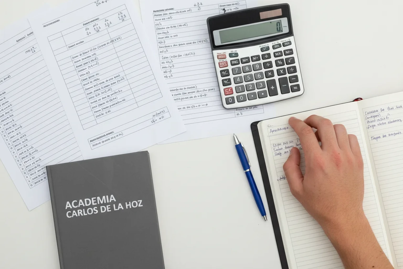 Vista cenital de mesa com simulacao de nota de candidatura, calculadora e libreta da Academia Carlos de la Hoz