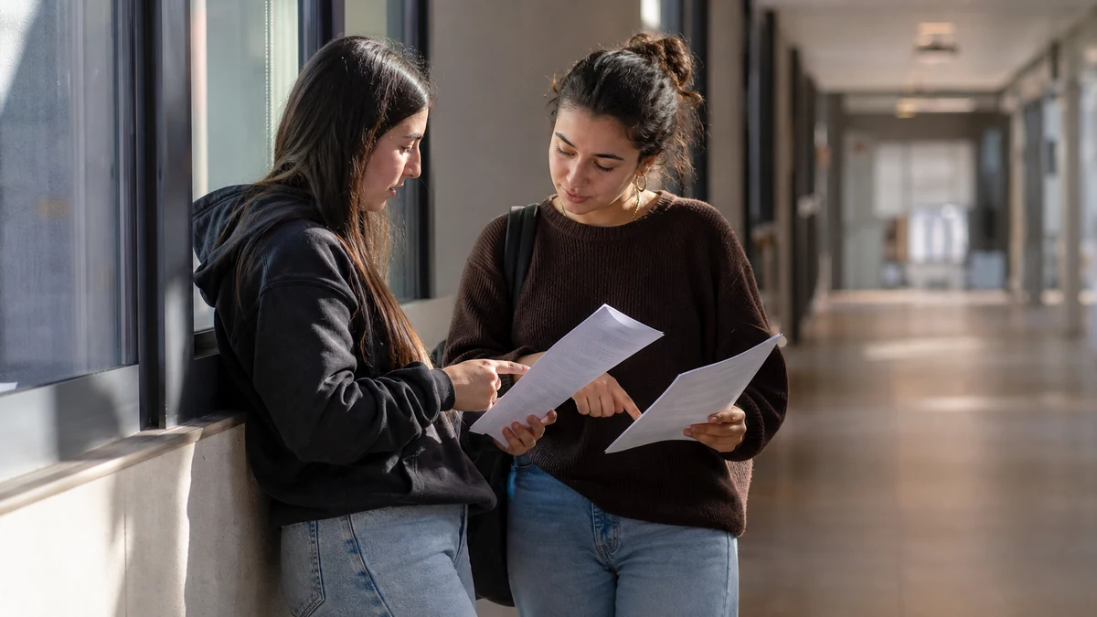 Dos estudiantes comparan los guiones de asignaturas distintas en un pasillo universitario